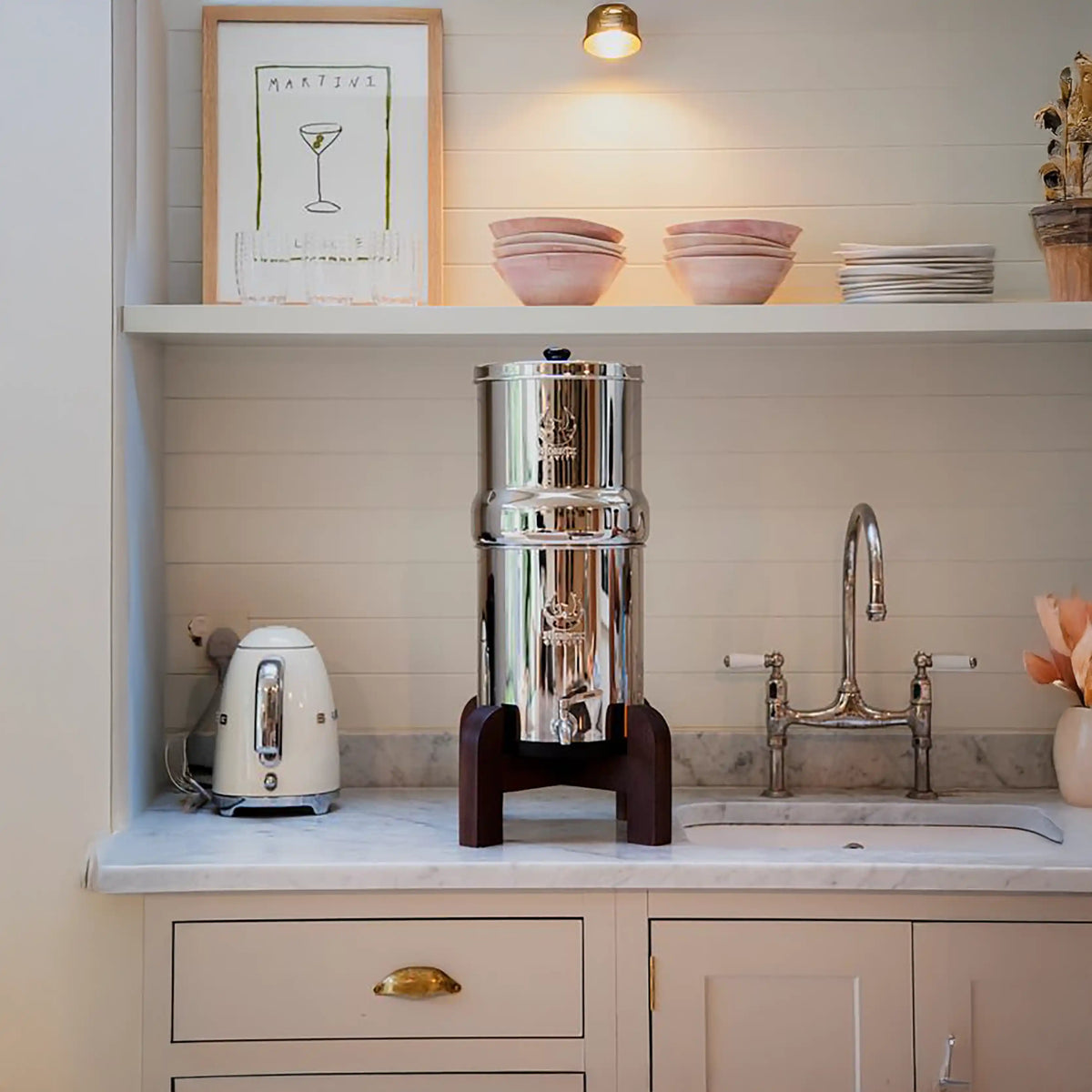 Stainless steel water filter on a kitchen counter with a sink and shelves in the background.